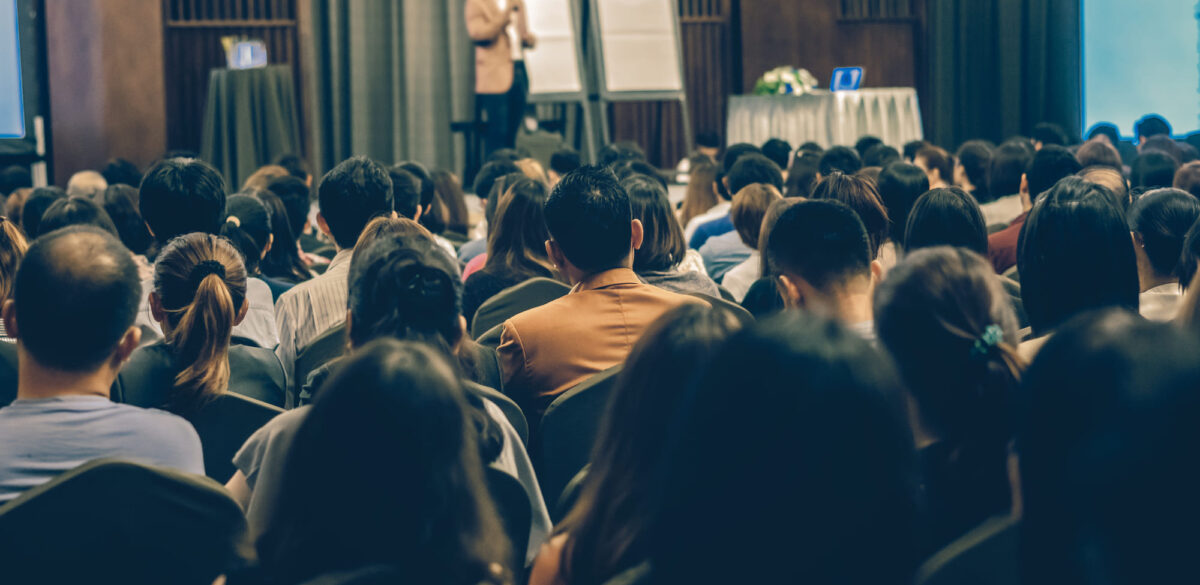 A group of event attendees sits and listens to a keynote speaker.