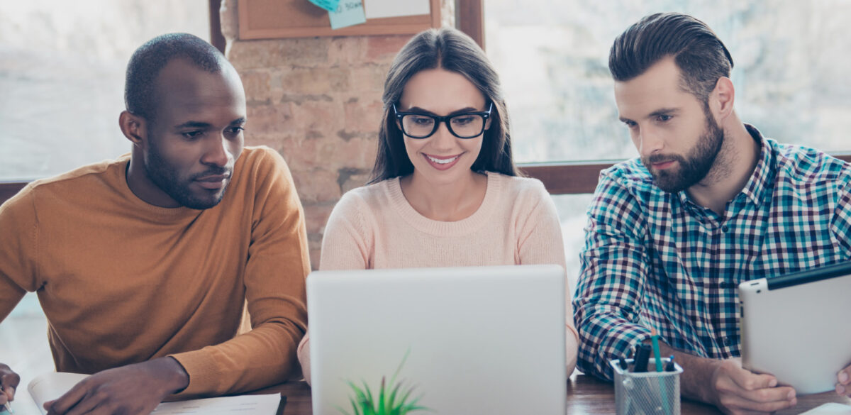 Three young professionals sitting at a table and looking at a laptop.